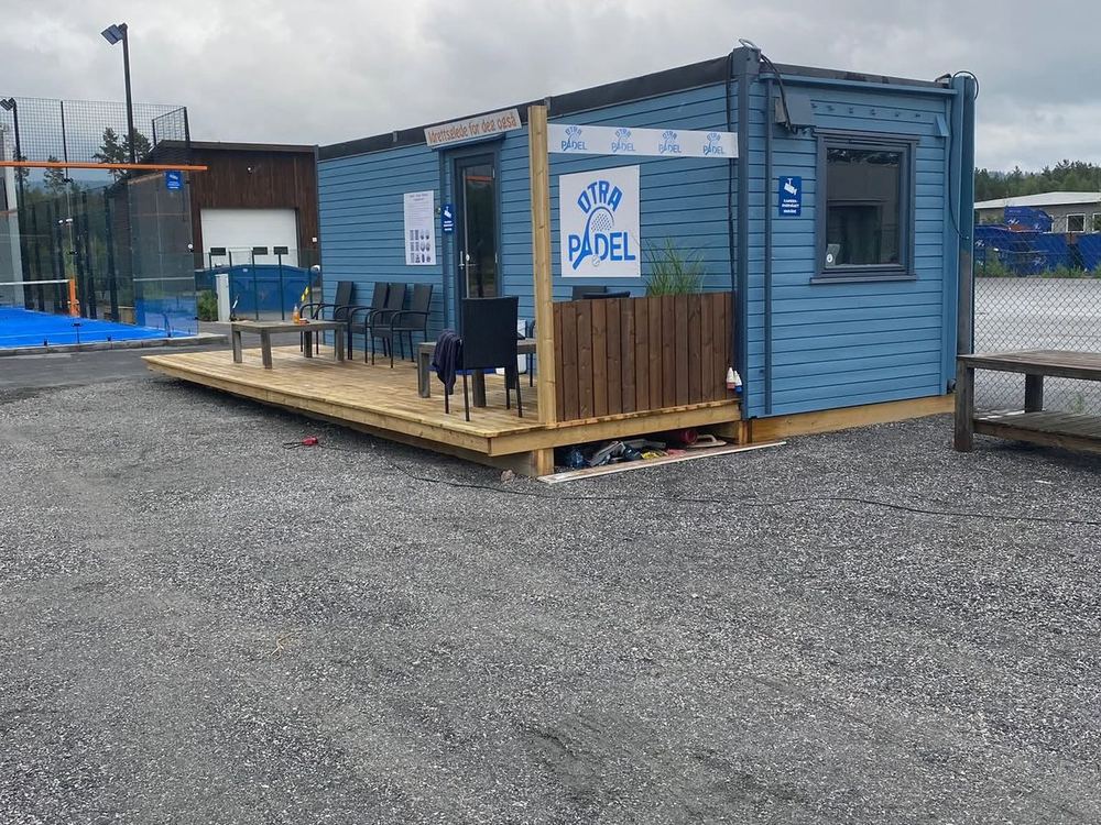 Det blå huset med terrasse og Otra Padel-skilt ved banen